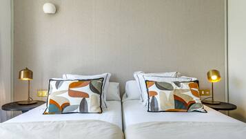 A hotel room with two beds, each with a patterned pillow, two bedside lamps, and a plain wall.