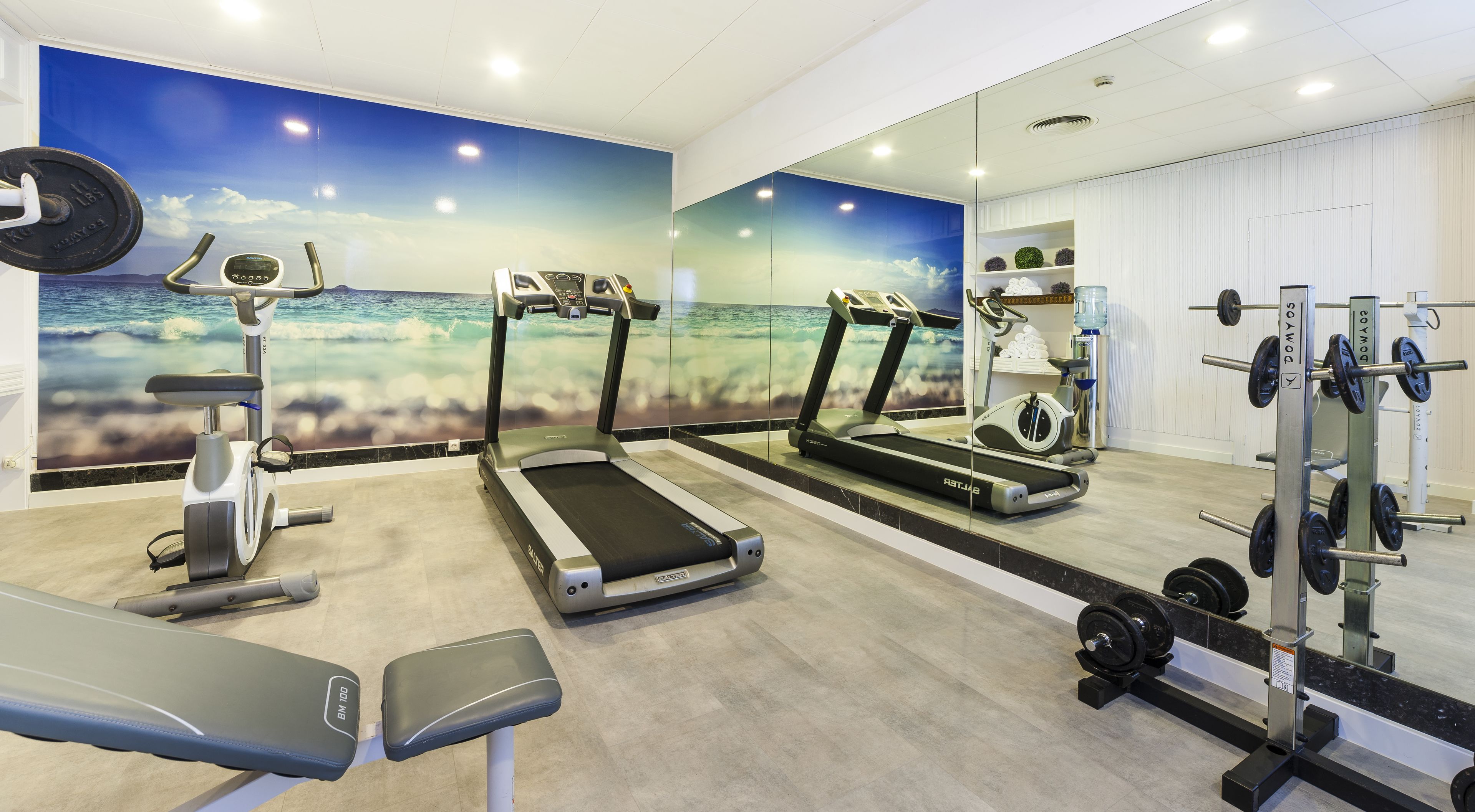 Un gimnasio con cintas de correr, una banca y un soporte para pesas.