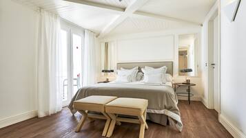 A bedroom with a large bed, two bedside tables, a bench, and a sliding glass door to the outside.