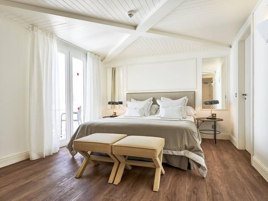 A bedroom with a large bed, two bedside tables, a bench, and a sliding glass door to the outside.