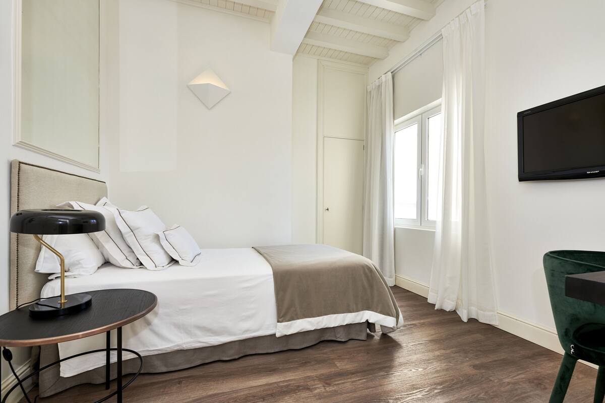 A hotel room with a bed, bedside table, lamp, and a television on the wall.