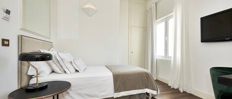 Una habitación de hotel con cama, mesita de noche, lámpara y televisión en la pared.