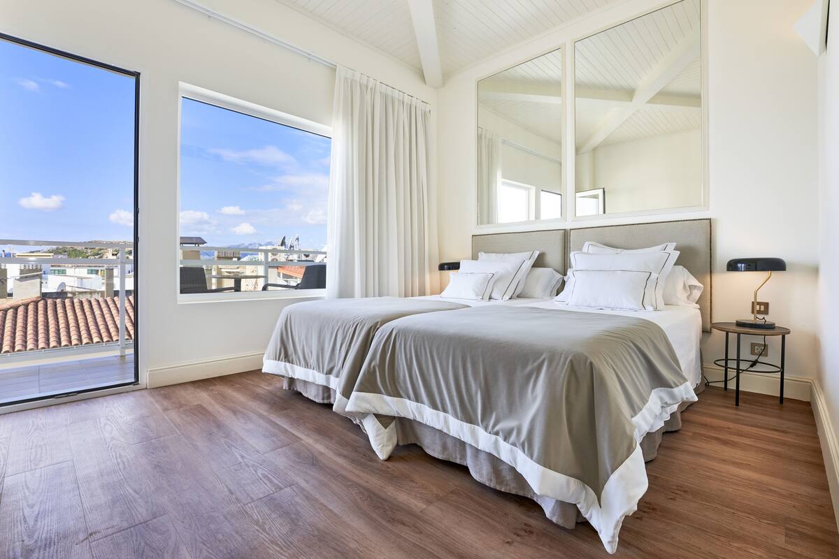 A bedroom with two beds, a large window, and a view of buildings.