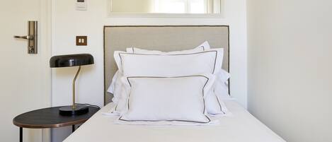 A neatly made bed with white linens and pillows, a bedside table with a lamp, and a door with a handle.
