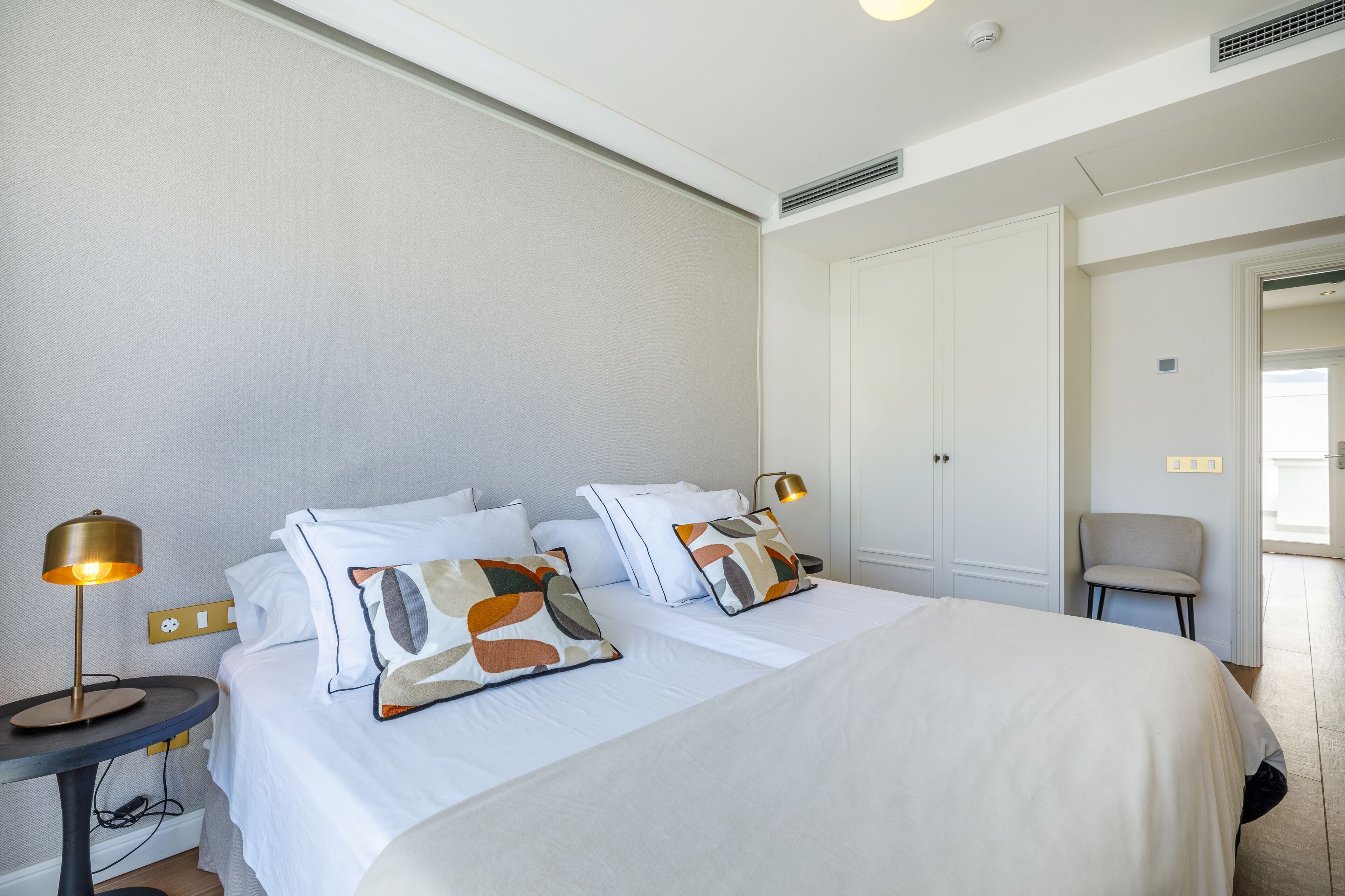 A hotel room with a large bed, two bedside tables, a chair, and a wardrobe.