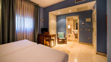 A hotel room with a bed, desk, chair, and a bathroom visible through an open door.