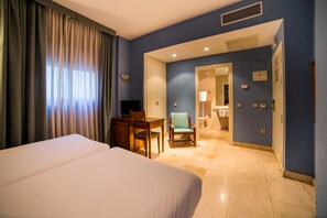 A hotel room with a bed, desk, chair, and a bathroom visible through an open door.