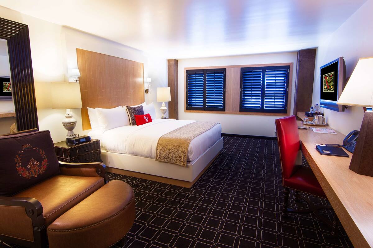 A hotel room with a bed, a desk, a chair, a TV, and a window with blinds.