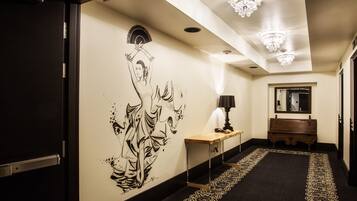 A hallway with a black and gold patterned carpet, a wooden console table with a lamp, and a wall mural.