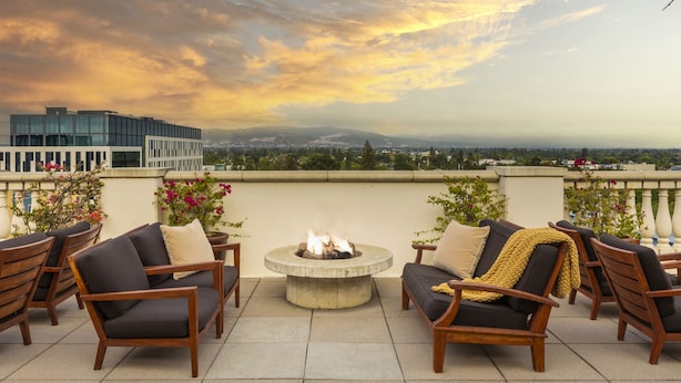 Eine Dachterrasse mit Sitzgelegenheiten im Freien, einer Feuerstelle und Blick auf die Stadt.