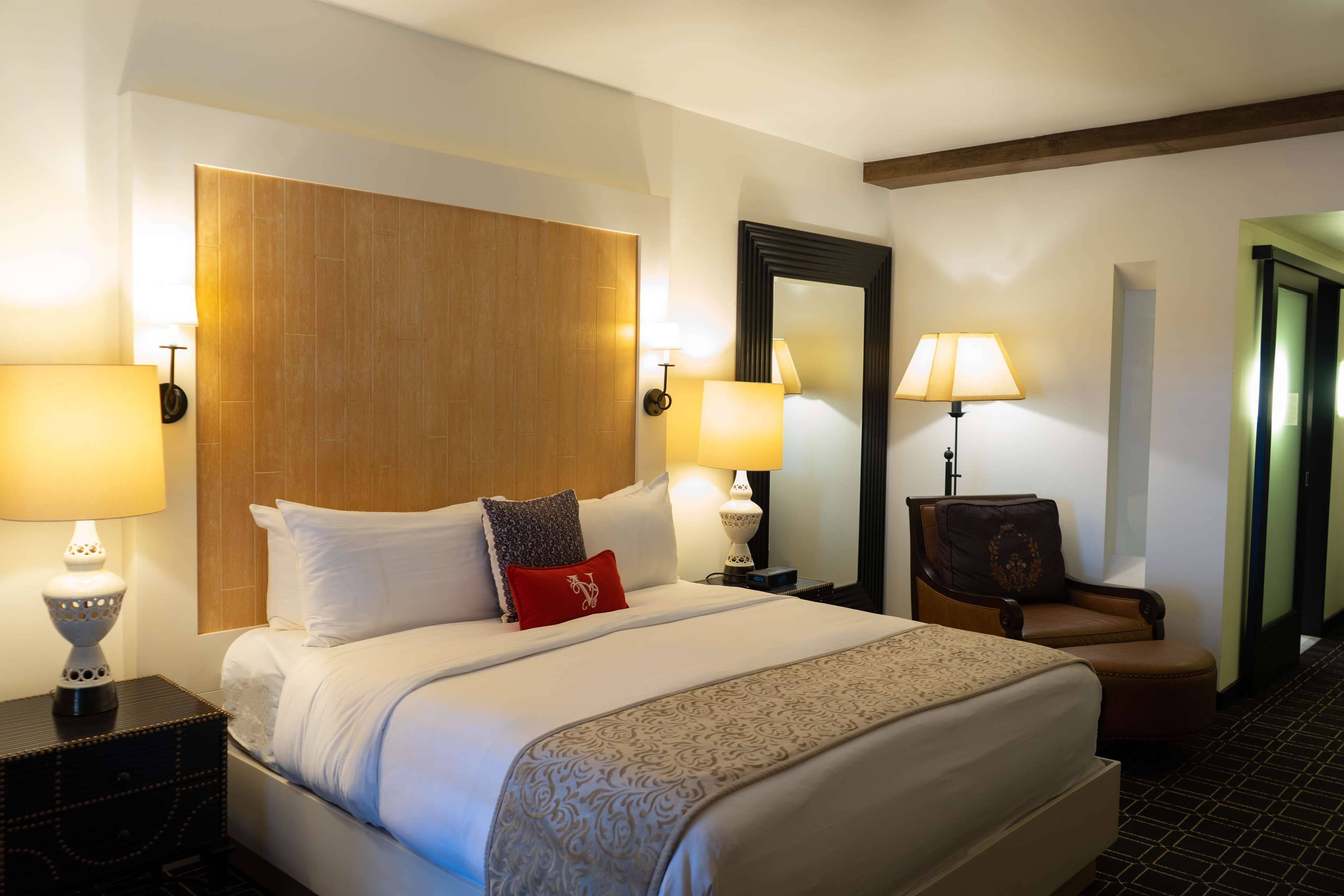A hotel room with a large bed, two bedside tables with lamps, a chair, and a mirror on the wall.