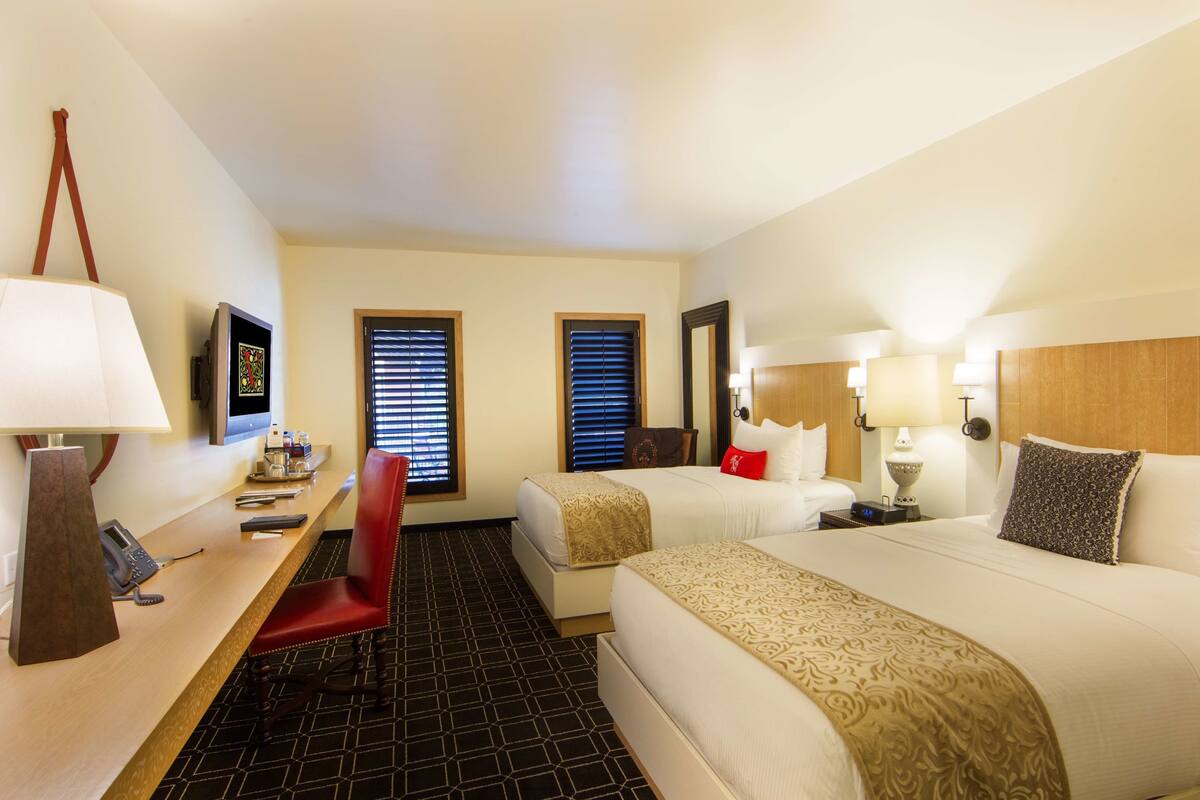 A hotel room with two beds, a desk with a telephone, a chair, and a TV.