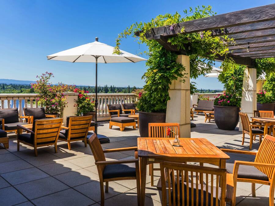 Eine Terrasse im Freien mit Holzmöbeln, einem weißen Sonnenschirm und Kübelpflanzen.