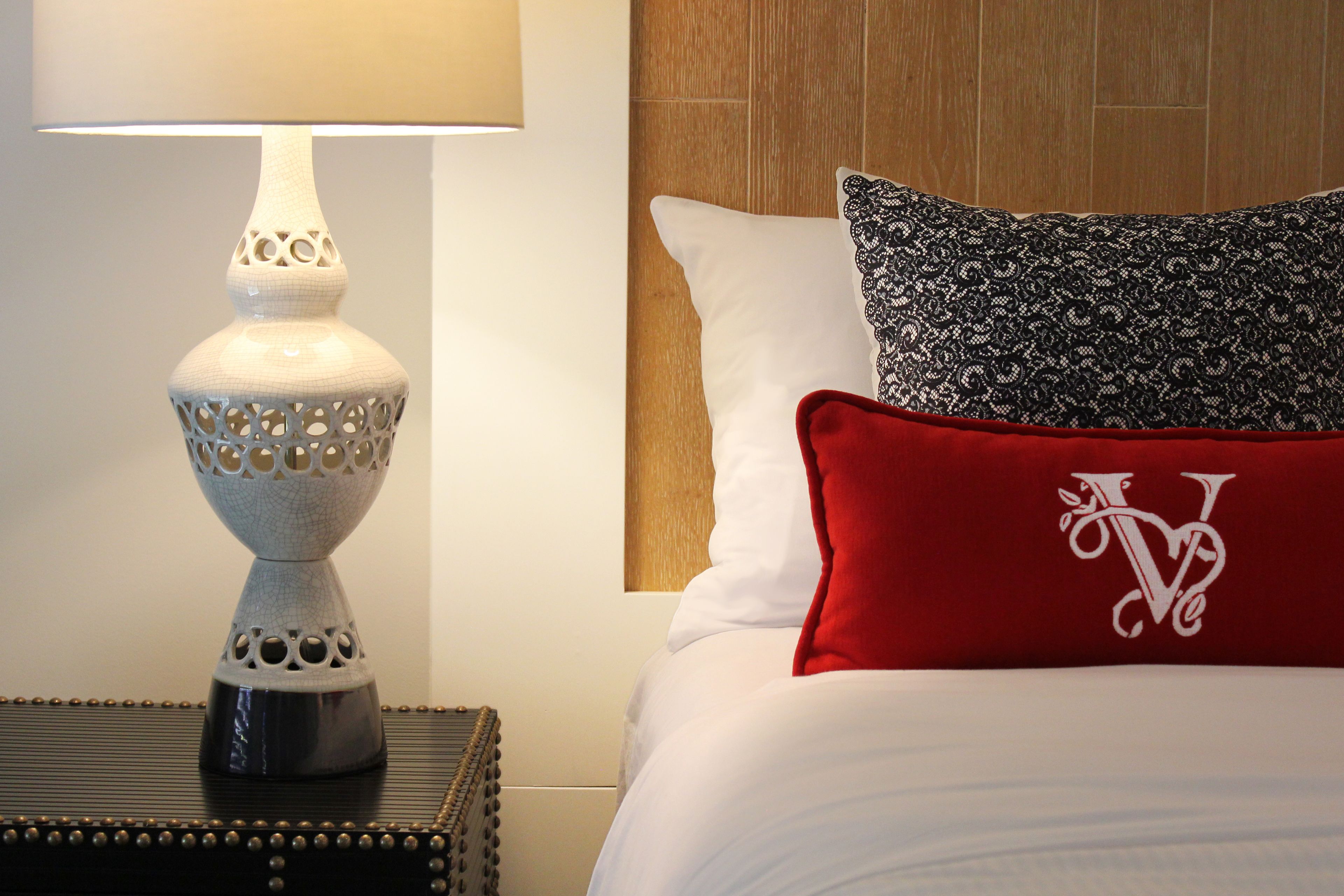 A neatly made bed with white and red pillows, a decorative lamp, and a wooden headboard.