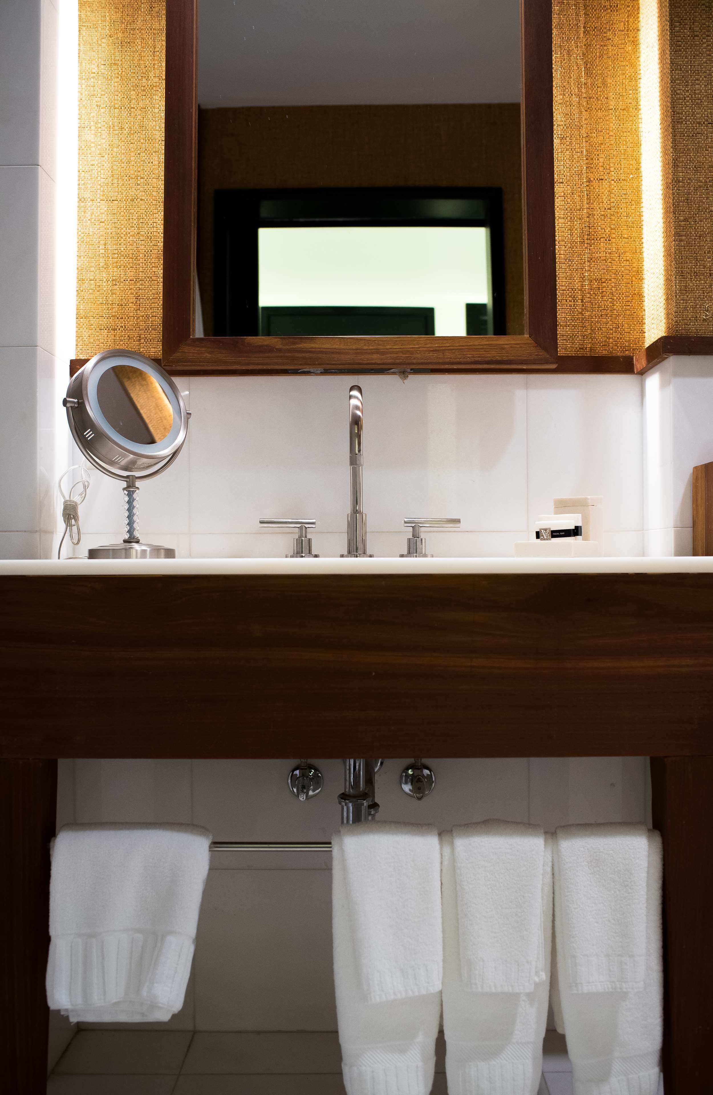 Un baño con un tocador de madera, un espejo, un lavabo y tres toallas colgadas.