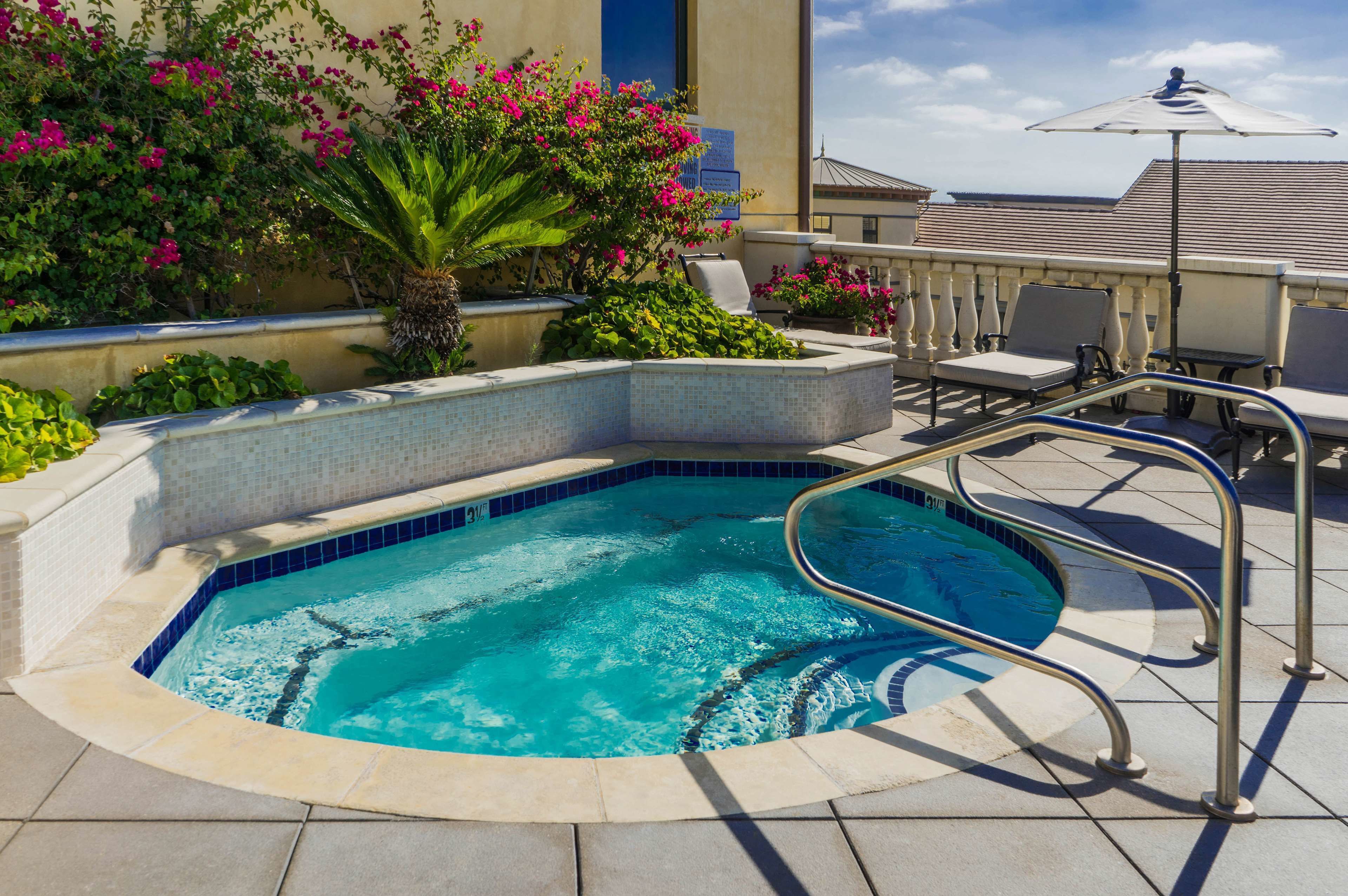 Une piscine dont le bord est recouvert de carrelage, entourée de chaises longues et d’un palmier.