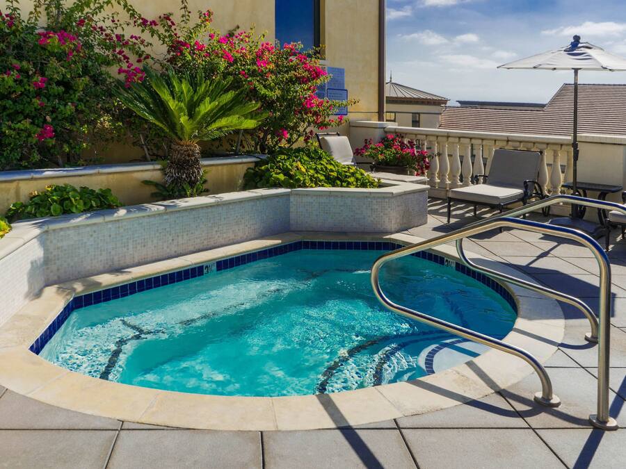 Une piscine dont le bord est recouvert de carrelage, entourée de chaises longues et d’un palmier.