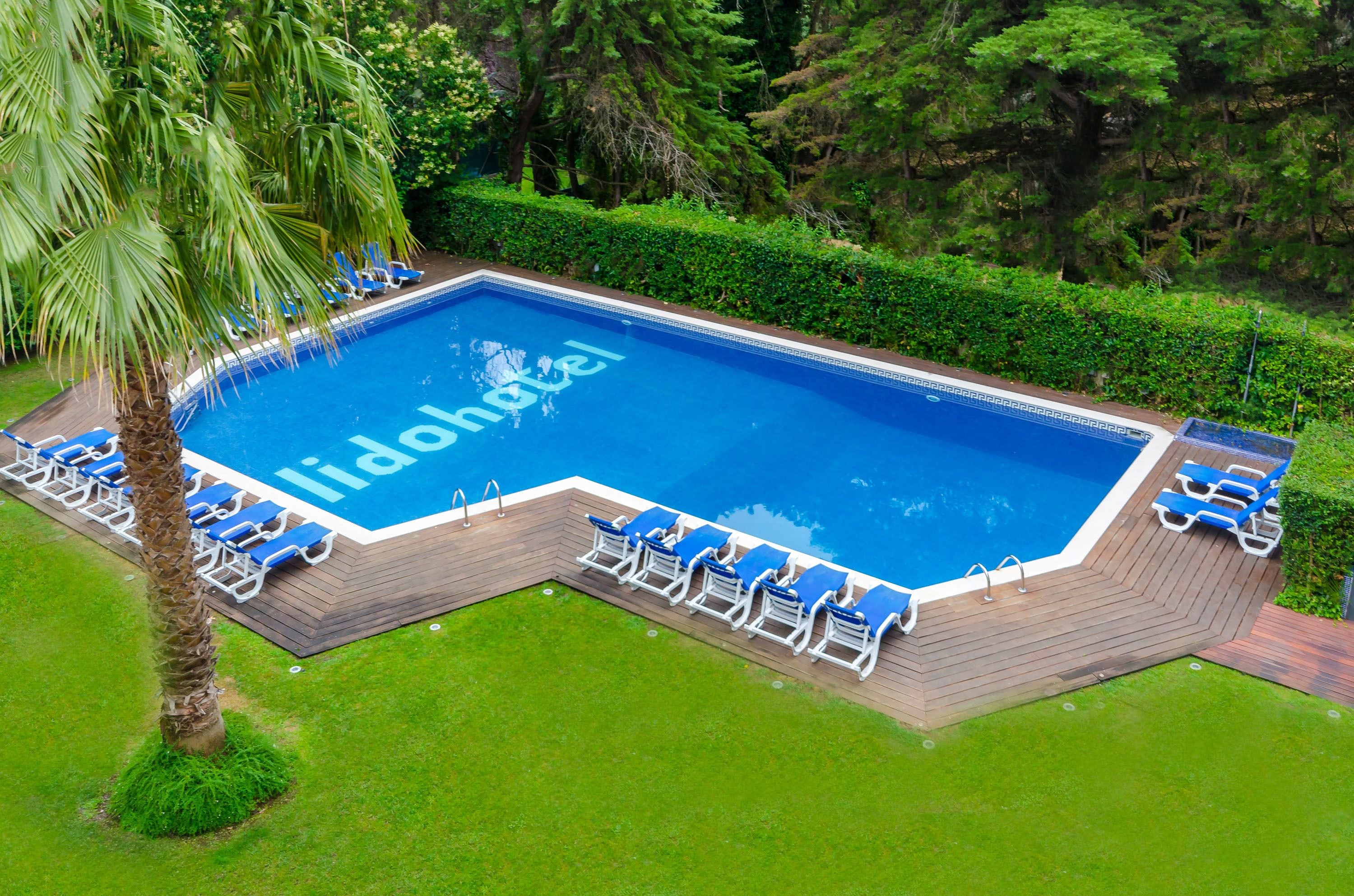 Une piscine sur laquelle est inscrit le mot « lidohotel », entourée de chaises longues bleues et d’une terrasse en bois.