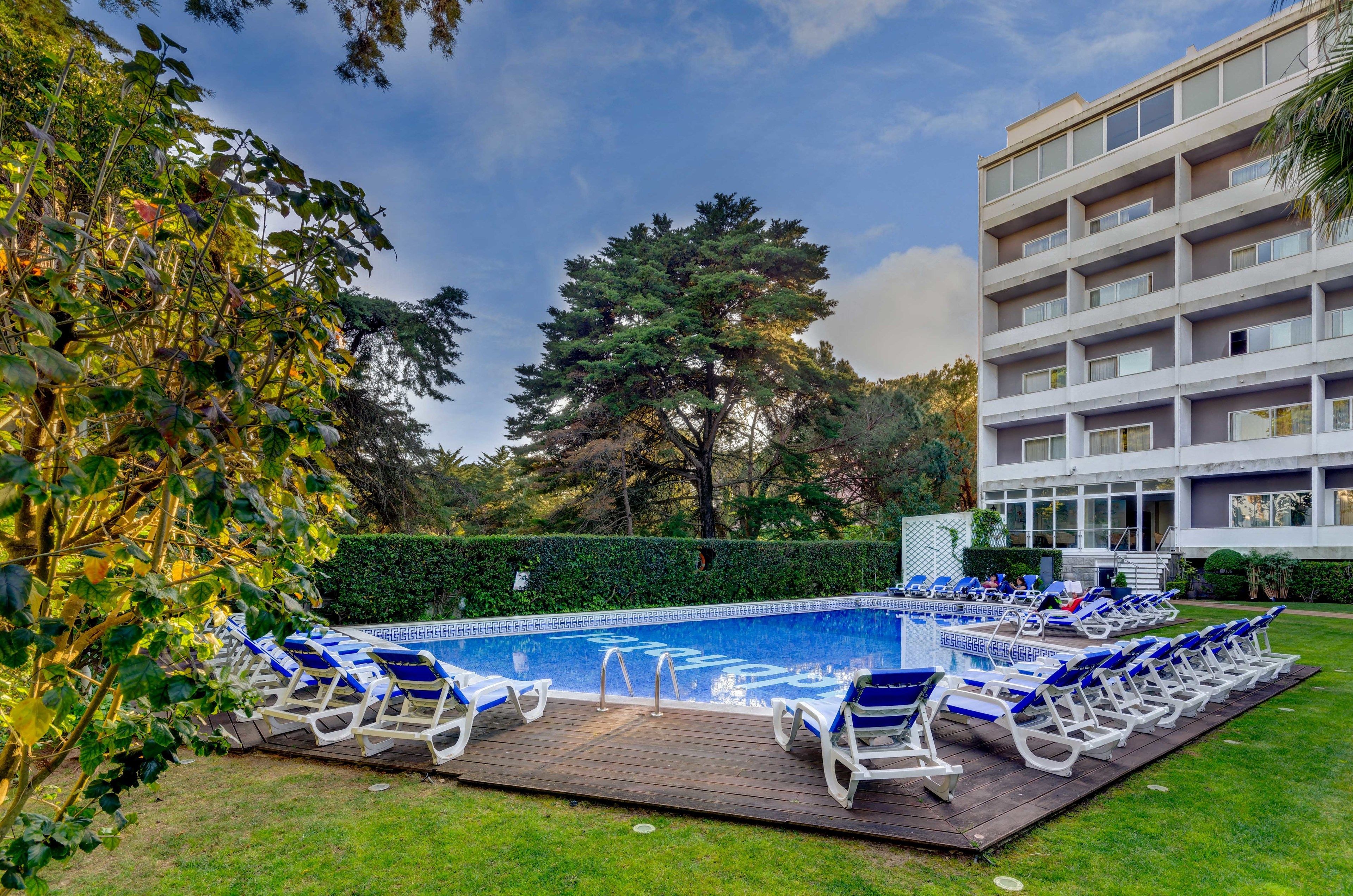 A swimming pool with lounge chairs, surrounded by greenery and a building with multiple floors.