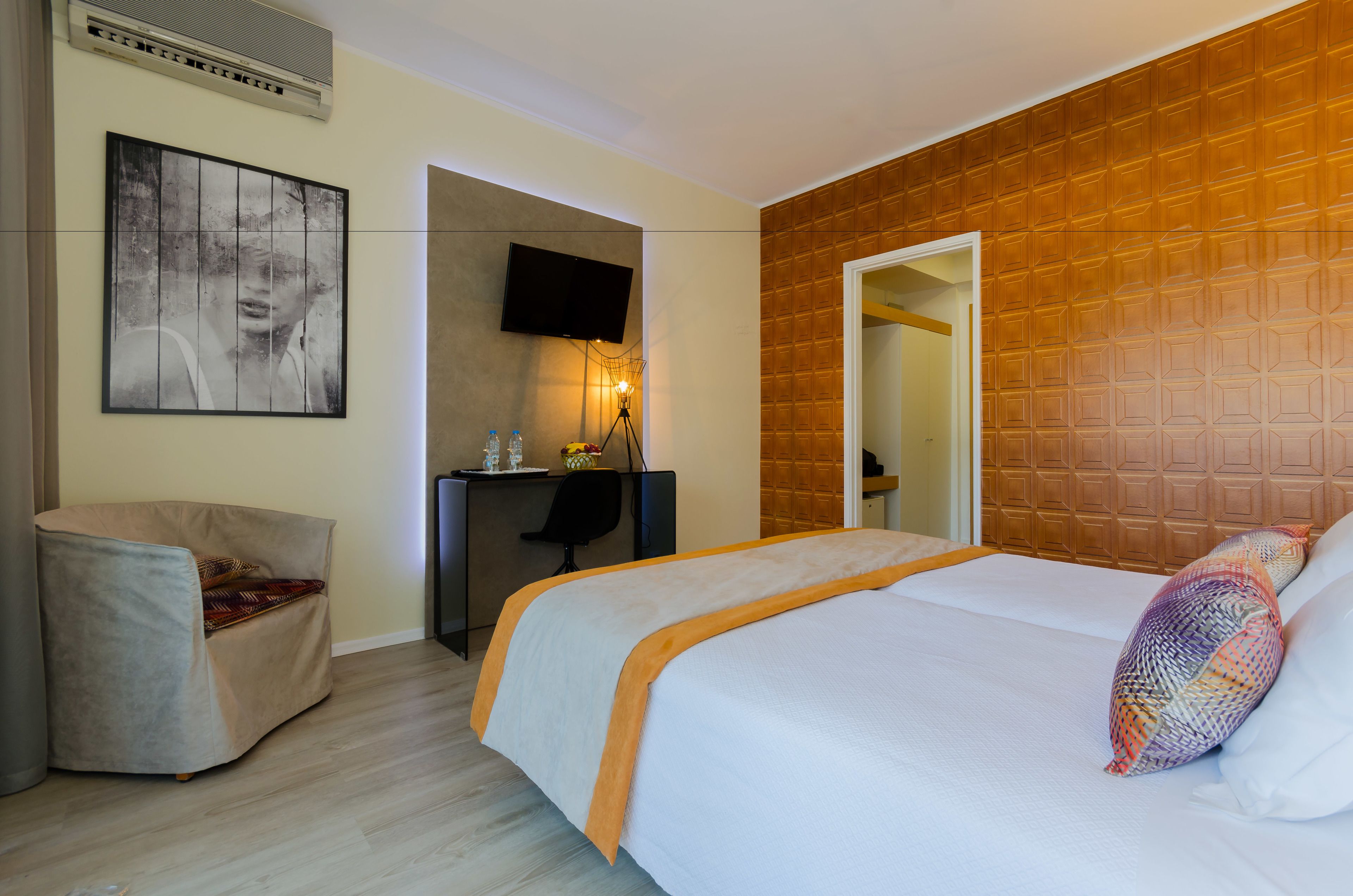 A hotel room with a bed, a desk, a chair, a TV, and a painting on the wall.