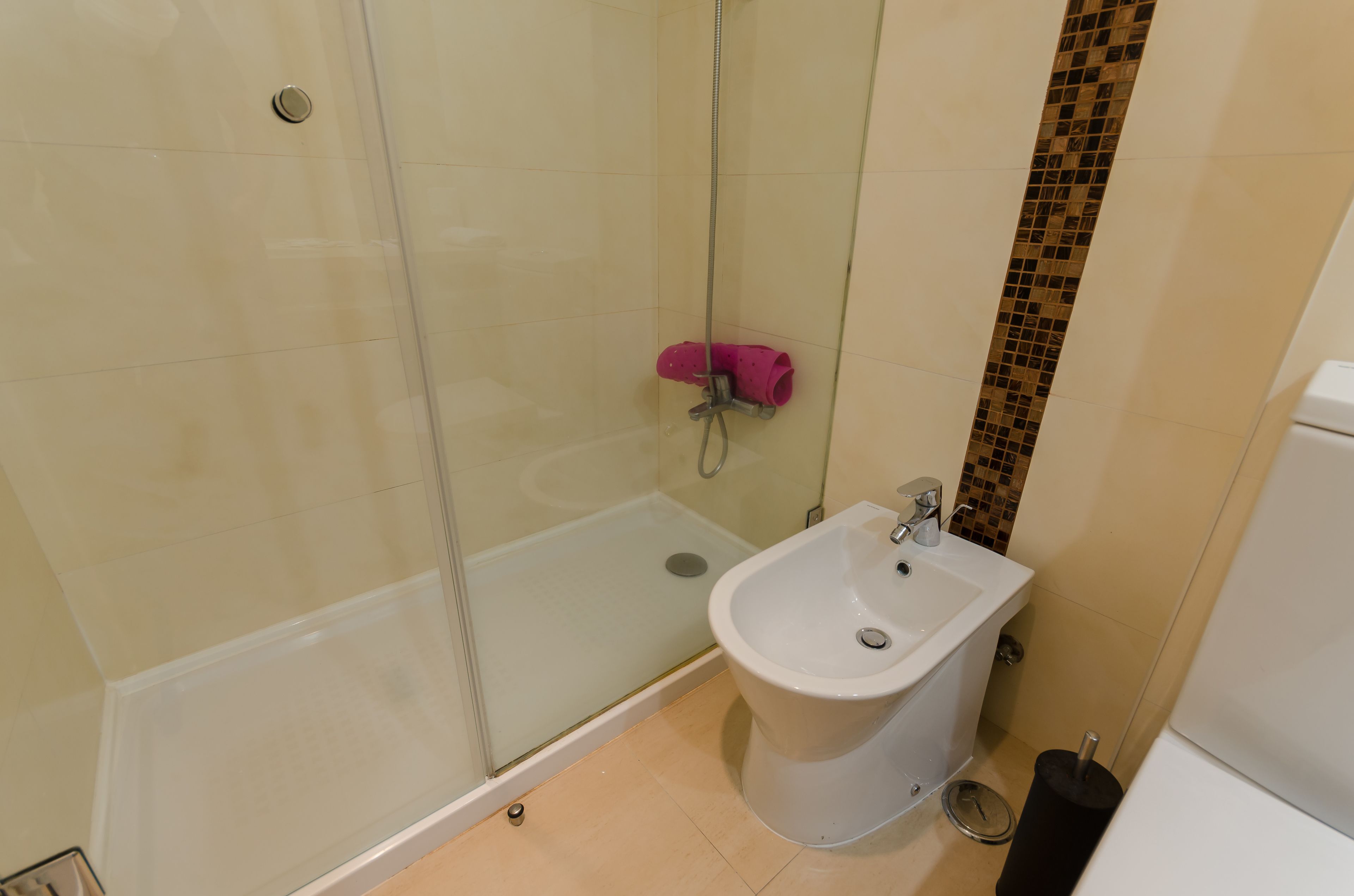 Un baño con cabina de ducha de vidrio, un lavamanos blanco y una pared de azulejos con diseño de mosaico.