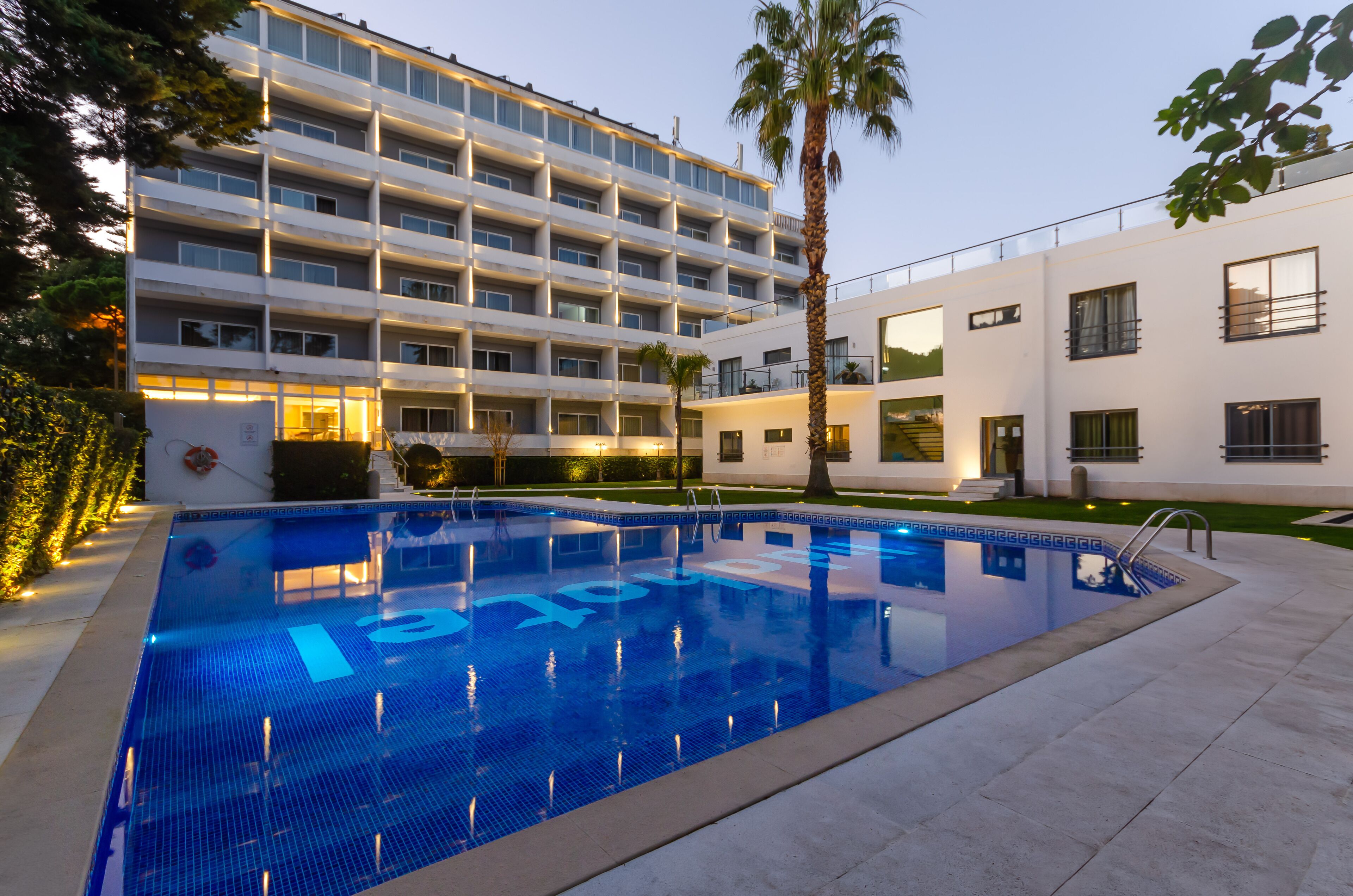 A modern hotel with a swimming pool, multiple floors, and a well-lit exterior.