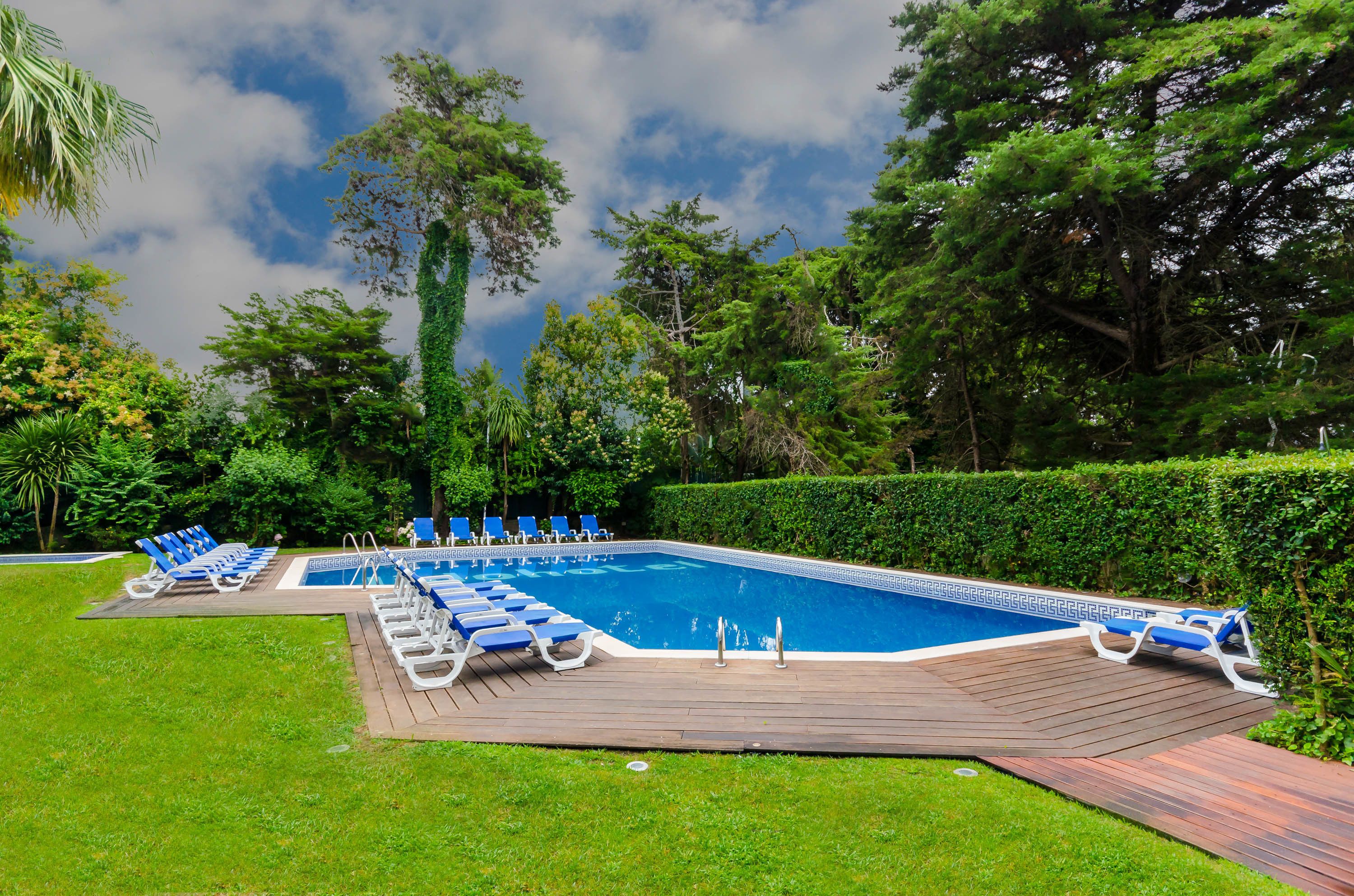 Una piscina rectangular con muelle de madera y sillas reclinables azules.