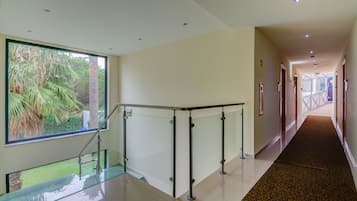 A modern hotel corridor with glass railings, a patterned carpet, and a view of greenery outside.