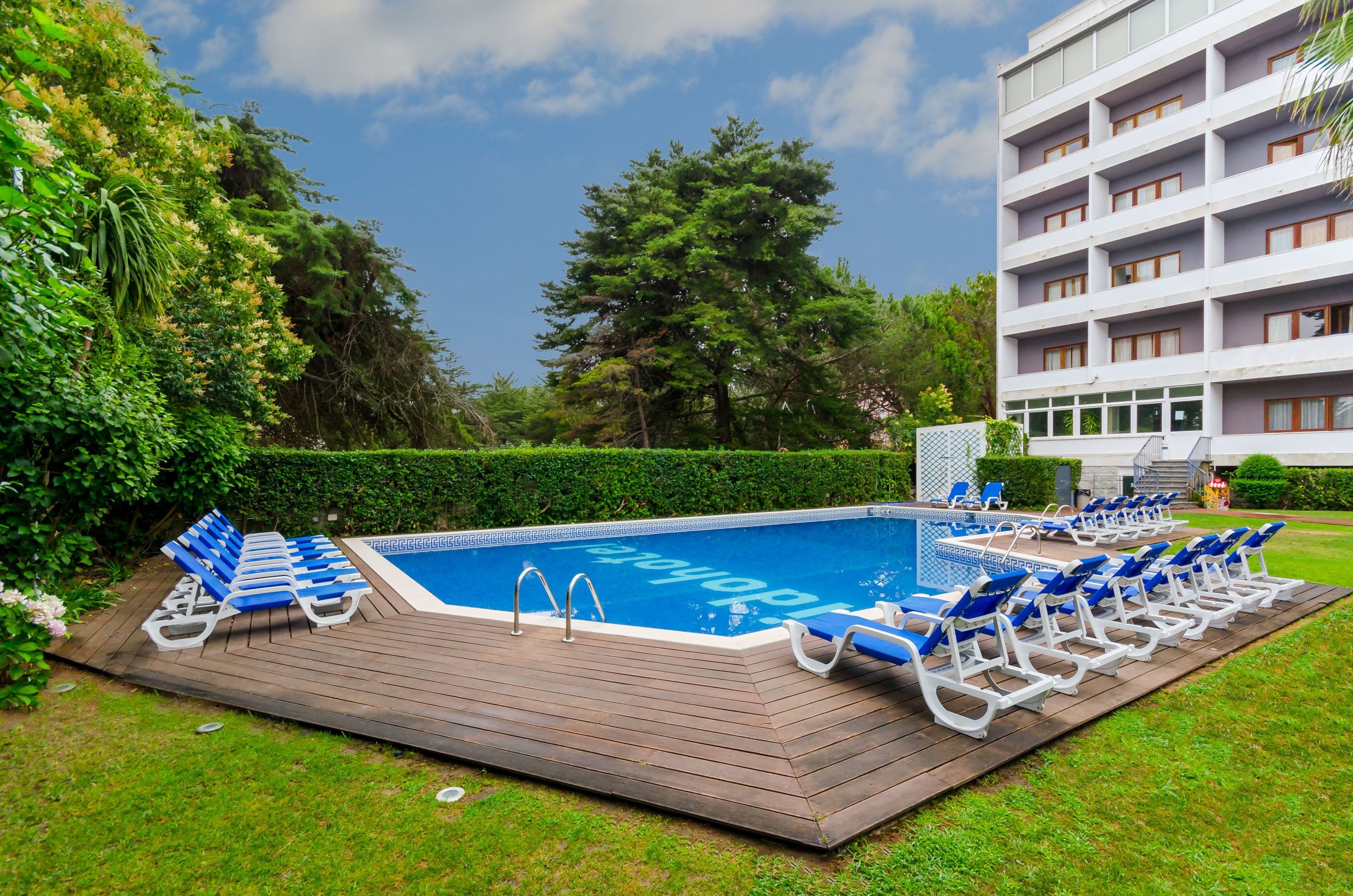 A swimming pool with lounge chairs, surrounded by greenery and a building with multiple floors.