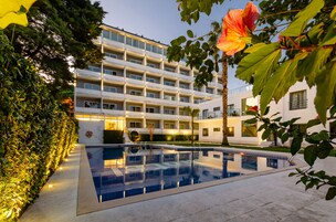 Un hotel moderno con piscina, rodeado de exuberante vegetación y un exterior bien iluminado.