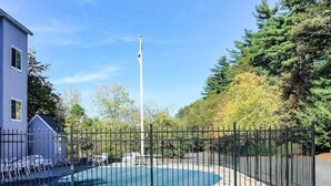 A two-story building with a swimming pool, surrounded by a fence, and a tall flagpole in the background. - Sturbridge Hotel (Sturbridge)