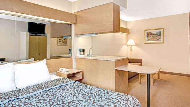 A hotel room with a bed, a desk, a chair, a mirror, a sink, and a painting on the wall. - Sturbridge Hotel (Sturbridge)