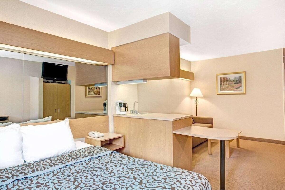 Une chambre d’hôtel avec un lit, un bureau, une chaise, un miroir, une télévision et un tableau au mur.