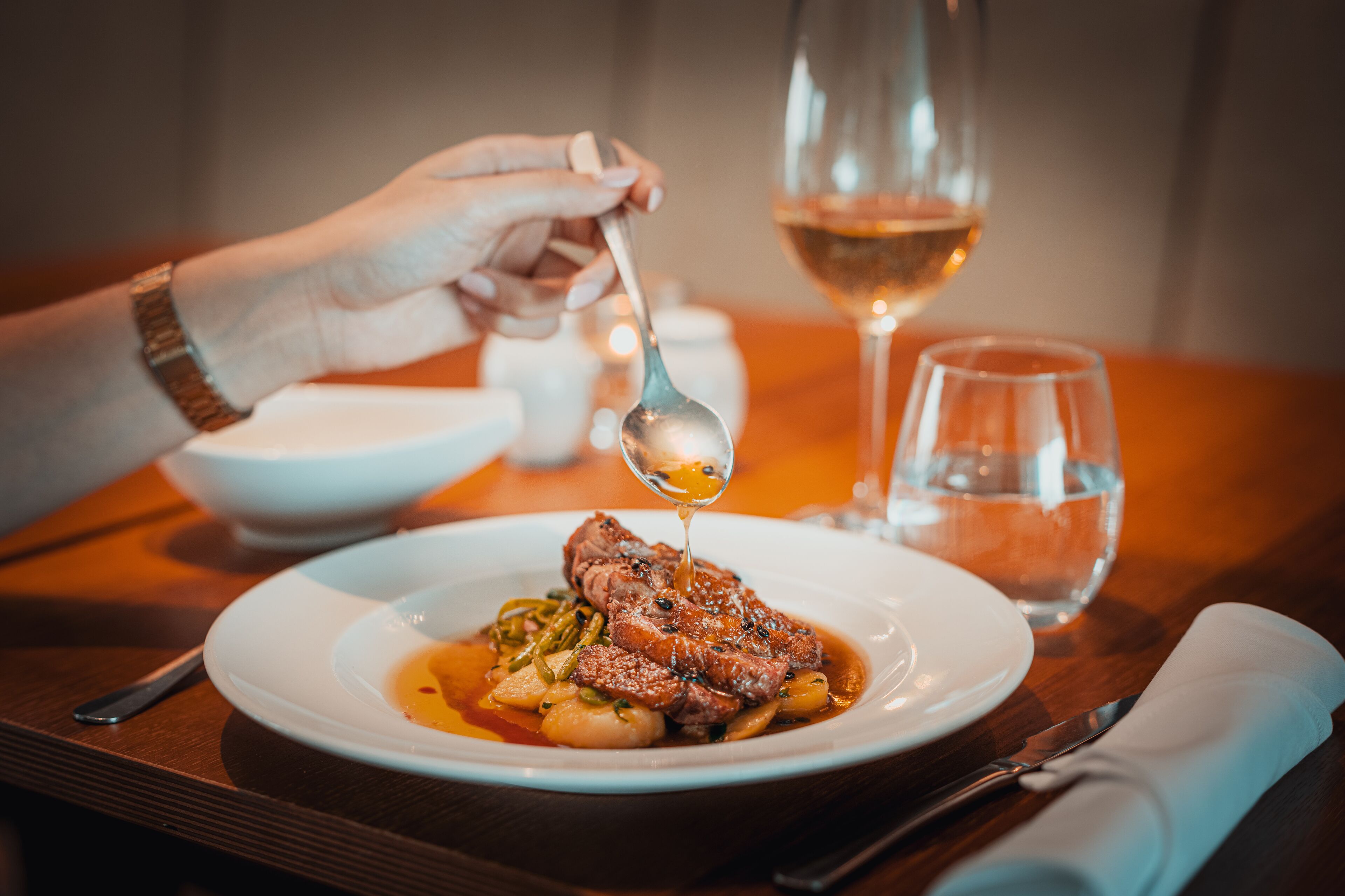 A dining table with a plate of food, a spoon, a glass of wine, and a candle.