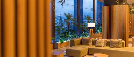 A modern lounge area with a sofa, round tables, and a large window with a view of palm trees.