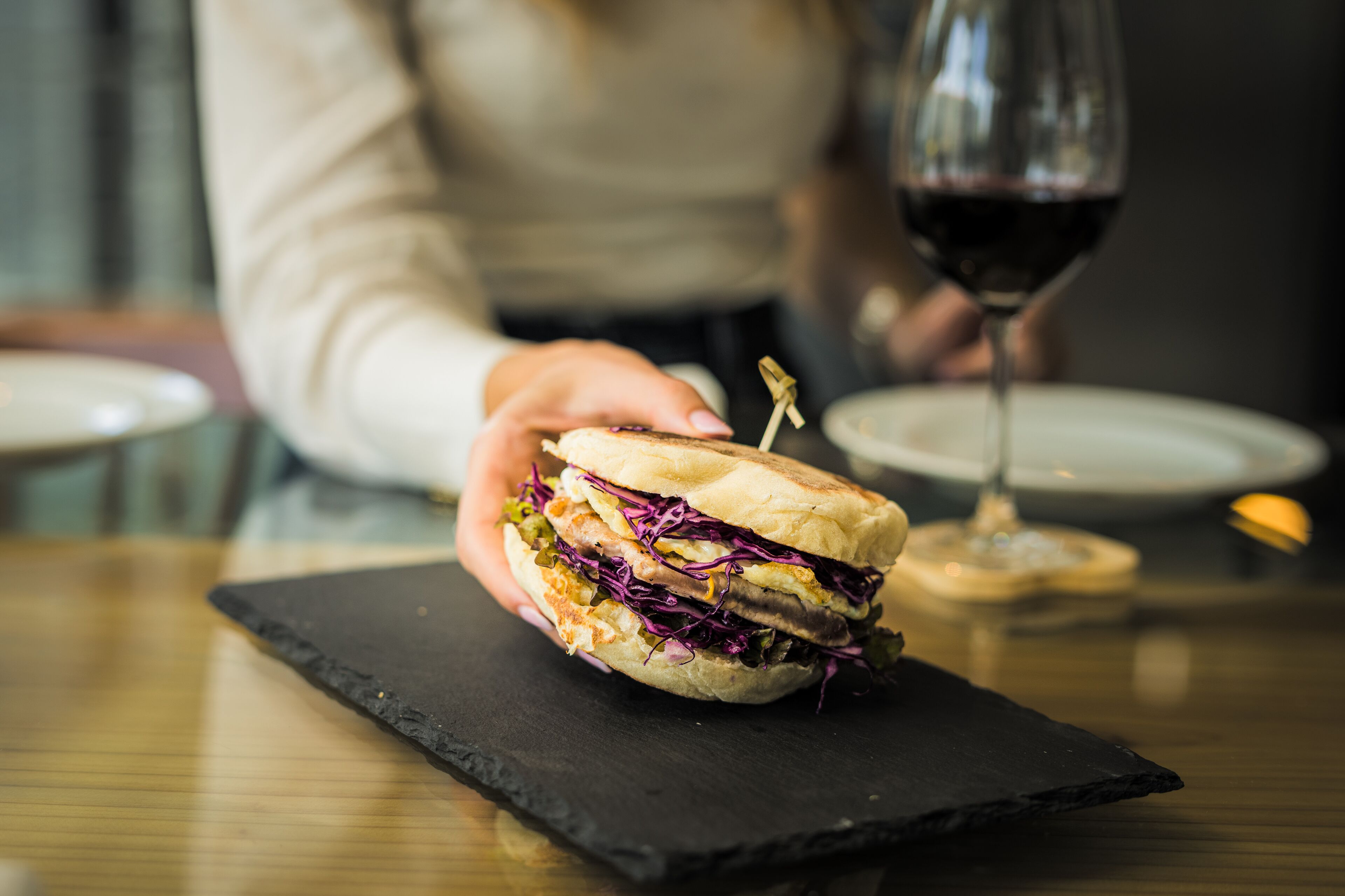A sandwich on a slate plate with a wine glass in the background.