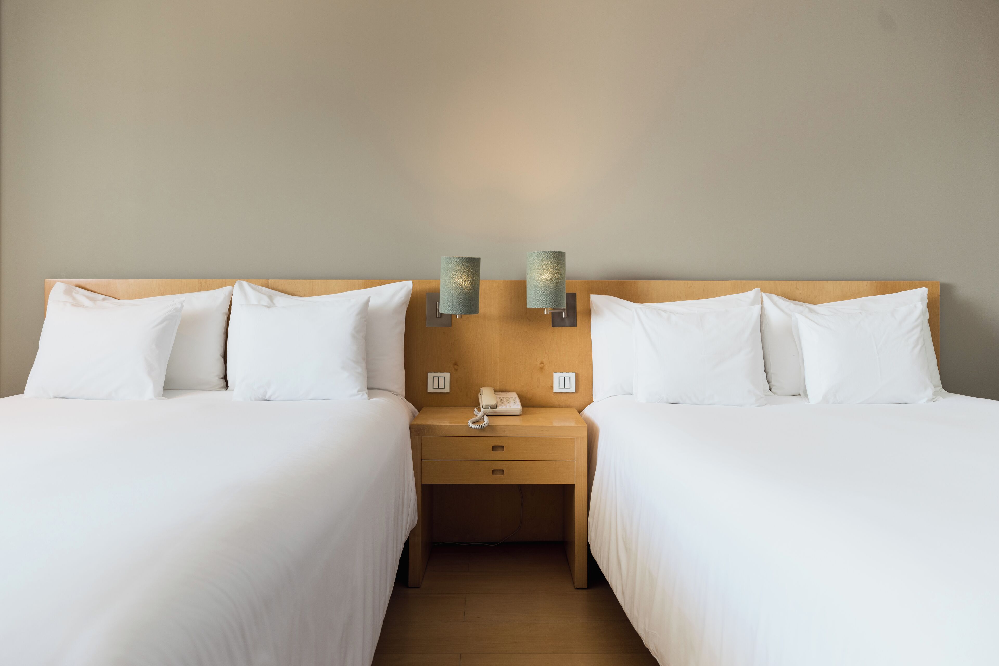A hotel room with two single beds, a wooden headboard, bedside tables with lamps, and a telephone.
