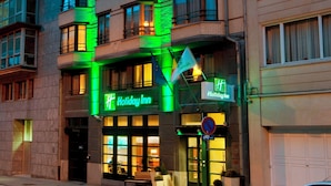 A multi-story building with a Holiday Inn sign, featuring a modern architectural design with large windows and a prominent green-lit facade.