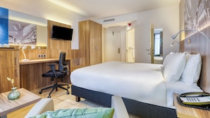 A hotel room with a large bed, a desk with a chair, a TV mounted on the wall, and a wooden wardrobe. - Holiday Inn Brussels Schuman by IHG (Brussels)