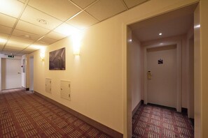 Un corridoio di un hotel con tappeto a motivi, illuminazione incassata, un quadro appeso e una porta con serratura.