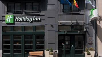 Fachada de un hotel Holiday Inn con un logotipo verde, una banca afuera y banderas.