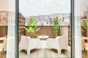 A balcony with two white chairs and a small table, surrounded by potted plants, overlooking a cityscape with buildings and a clear sky. - Holiday Inn Brussels Schuman by IHG (Brussels)