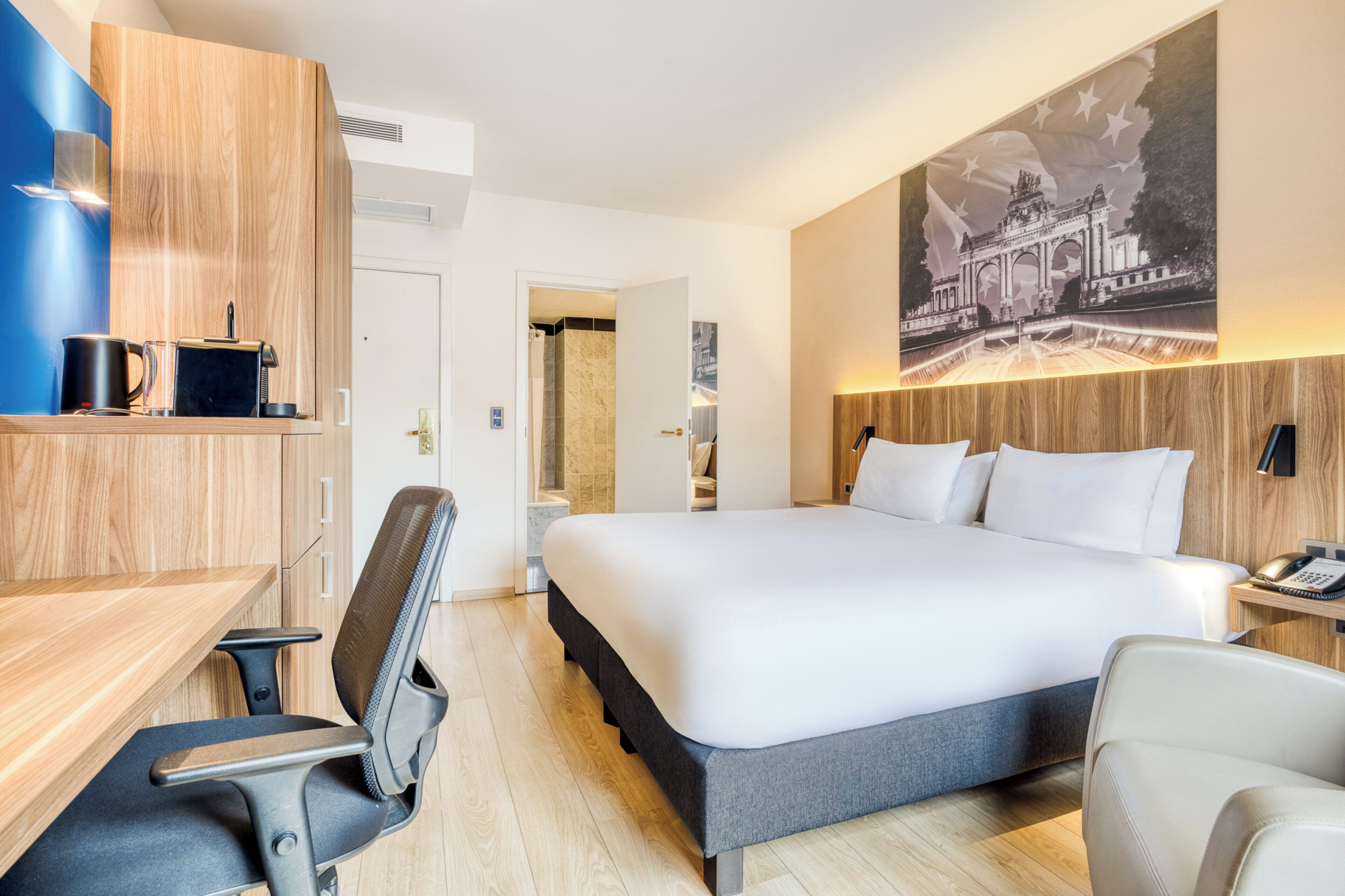 Habitación de hotel con una cama grande, un escritorio con silla, un teléfono y un cuadro en la pared.
