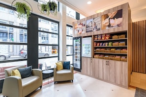 A modern interior with seating, a refrigerator, and snack shelves. - Holiday Inn Brussels Schuman by IHG (Brussels)