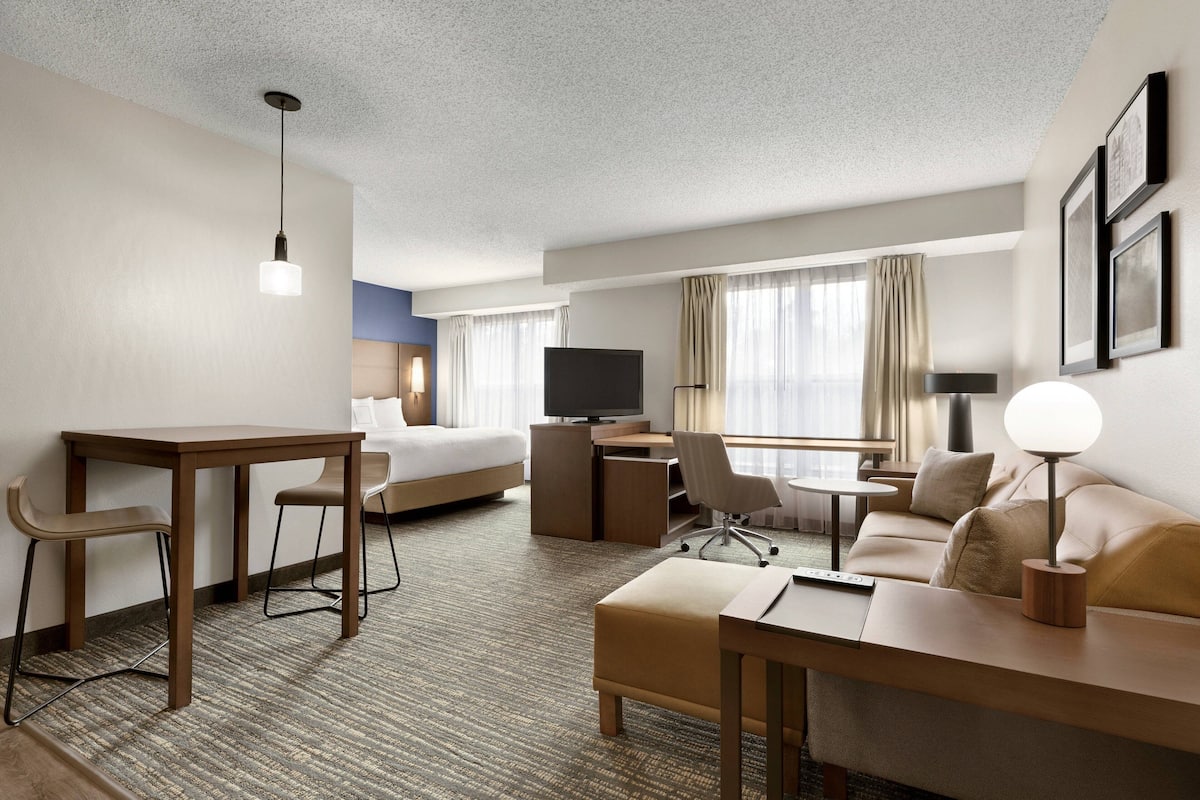 A hotel room with a bed, a desk, a TV, a sofa, and a lamp.