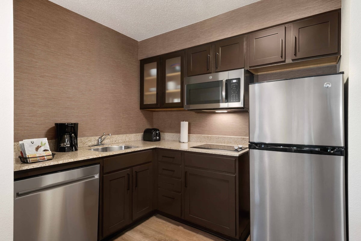 A modern kitchen with stainless steel appliances, dark wooden cabinets, and a granite countertop.