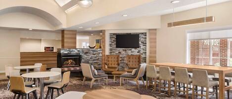 A hotel lobby with round tables, chairs, a fireplace, a TV, and a brick wall.