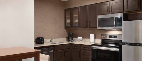 A compact kitchen with dark wooden cabinets, a stainless steel microwave, a coffee maker, and a refrigerator.