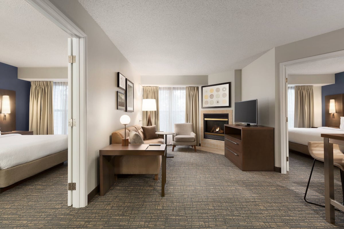 A hotel room with two beds, a desk, a chair, a TV, and a fireplace.