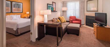 A hotel room with a bed, a sofa, a TV, and a fireplace.